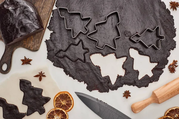 Vue du dessus de la pâte crue pour biscuits de Noël au chocolat sur fond blanc près de l'anis, couteau et rouleau à pâtisserie — Photo de stock