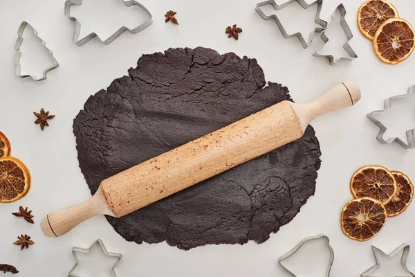 Vue du dessus de la pâte crue pour biscuits de Noël au chocolat avec rouleau à pâtisserie sur fond blanc près de l'anis, moules à pâte et agrumes séchés — Photo de stock