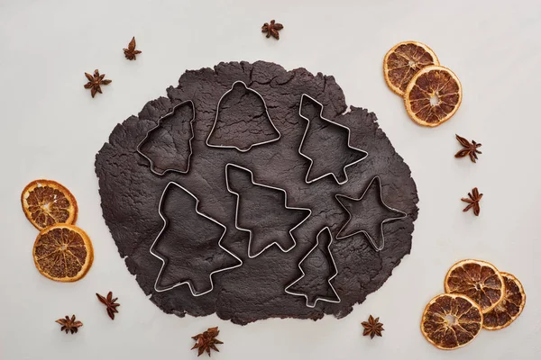 Vista dall'alto della pasta cruda per biscotti di Natale al cioccolato con stampi per pasta su sfondo bianco vicino all'anice e agli agrumi secchi — Foto stock