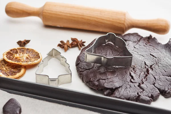 Pâte crue pour biscuits de Noël au chocolat près de rouleau à pâtisserie et moules à pâte sur fond blanc — Photo de stock