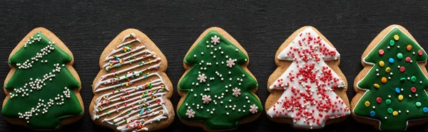 Flat lay with delicious glazed Christmas tree cookies on black wooden table, panoramic shot — Stock Photo