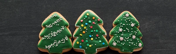 Flat lay with delicious glazed Christmas tree cookies on black wooden table, panoramic shot — Stock Photo