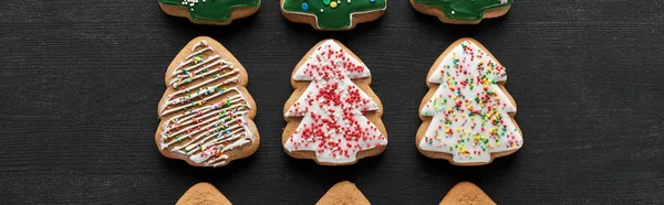 Flat lay with delicious glazed Christmas tree cookies on black background, panoramic shot — Stock Photo