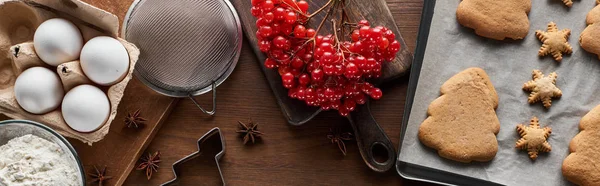 Top view of Christmas cookies near ingredients, dough molds and viburnum on wooden table, panoramic shot — Stock Photo