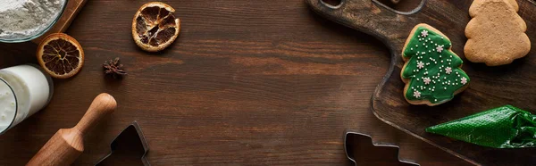 Top view of glazed Christmas cookies near ingredients on wooden table, panoramic shot — Stock Photo