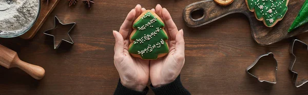 Vista ritagliata della donna che tiene il biscotto dell'albero di Natale al tavolo di legno, colpo panoramico — Foto stock
