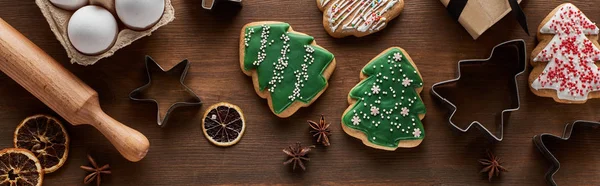 Vue du dessus des biscuits de Noël, des moules à pâte, des œufs et du rouleau à pâtisserie sur une table en bois, vue panoramique — Photo de stock