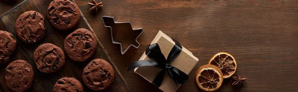 Top view of chocolate Christmas cookies near gift box on wooden table, panoramic shot — Stock Photo