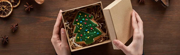 Vista ritagliata della scatola di apertura della donna con biscotto dell'albero di Natale al tavolo di legno, colpo panoramico — Foto stock