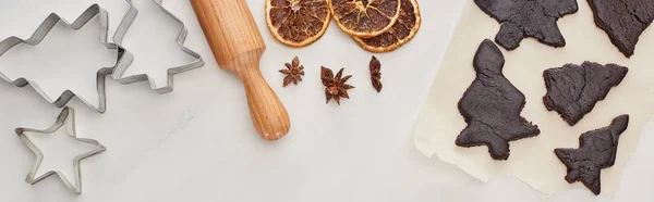 Top view of raw dough for chocolate Christmas cookies with rolling pin on white background near anise, dough molds and dried citrus, panoramic shot — Stock Photo