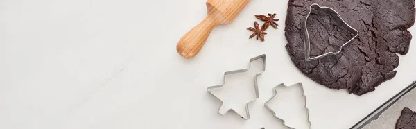 Vista dall'alto della pasta cruda per biscotti di Natale al cioccolato vicino al mattarello e stampi per pasta su sfondo bianco, colpo panoramico — Foto stock