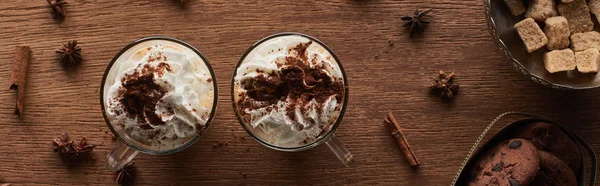 Вид на рождественское какао со взбитыми сливками на деревянном столе рядом с печеньем и коричневым сахаром, панорамный снимок — стоковое фото
