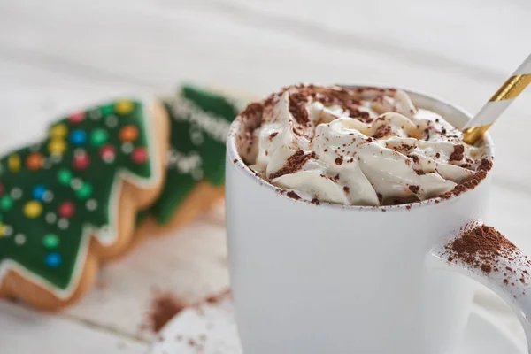 Selektiver Schwerpunkt von Weihnachtskakao mit Kakaopulver und Schlagsahne im Becher mit Stroh in der Nähe von Keksen — Stockfoto