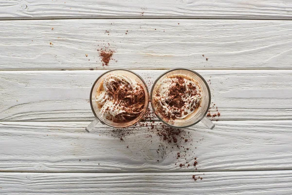 Top view of cacao with whipped cream and cacao powder in mugs on white wooden table — Stock Photo