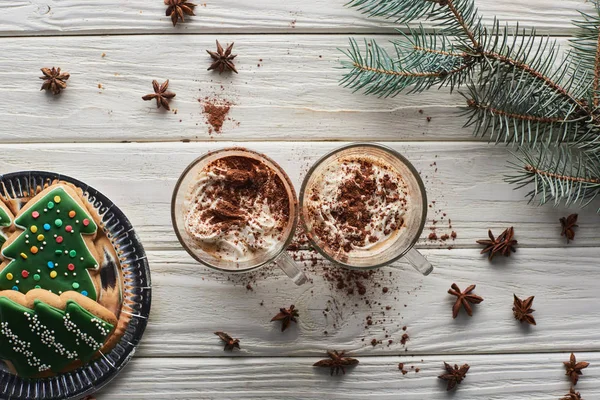 Вид зверху какао в кухольках на білому дерев'яному столі з ялиновим гілкою, анісом та різдвяним печивом — стокове фото