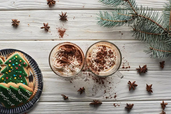 Top view of cacao in mugs on white wooden table with fir branch, anise and Christmas cookies — Stock Photo