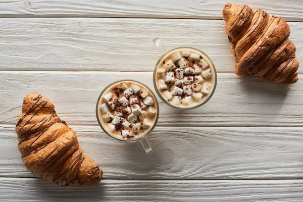 Vista superior del cacao con malvavisco cerca de galletas y croissants en mesa de madera blanca - foto de stock