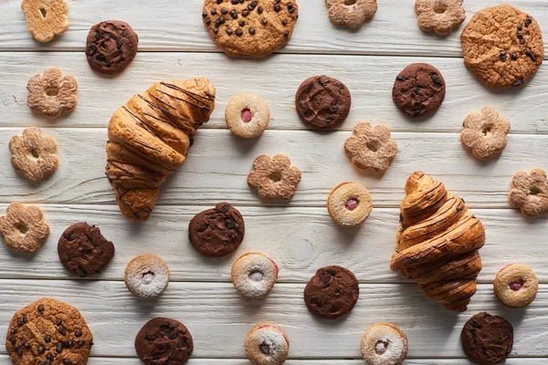 Draufsicht auf süße Kekse und Croissants auf weißem Holztisch — Stockfoto
