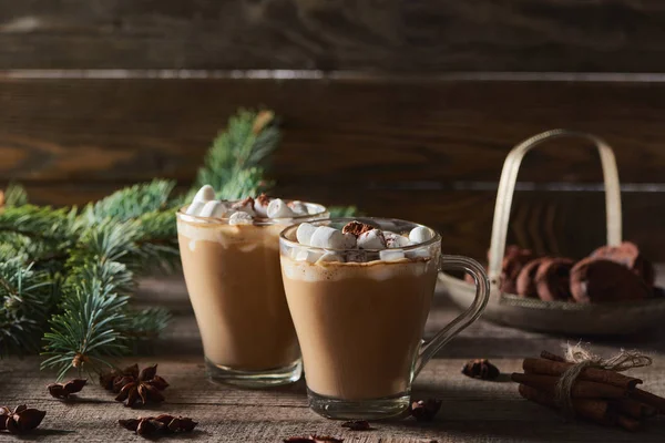 Focus selettivo di cacao con marshmallow e cacao in polvere in tazze vicino a rami di pino, cannella e anice su tavolo di legno — Foto stock