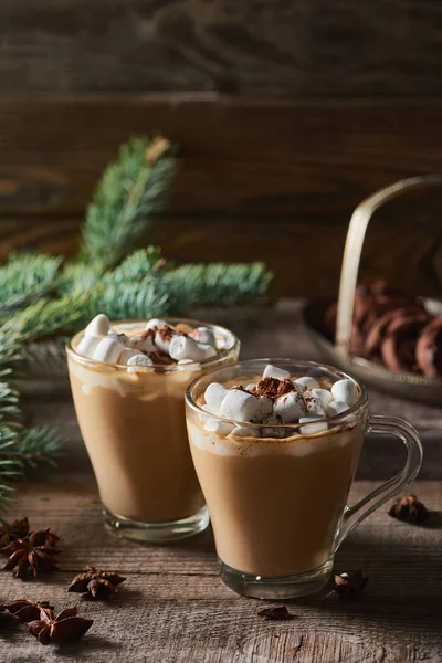 Focus selettivo di cacao con marshmallow e cacao in polvere in tazze vicino a rami di pino, cannella e anice su tavolo di legno — Foto stock