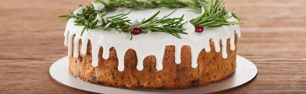 Вкусный рождественский пирог с белой глазурью, розмарином и клюквой на тарелке на деревянном столе — стоковое фото
