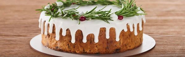 Tasty christmas pie with white icing, rosemary and cranberries on plate on wooden table — Stock Photo