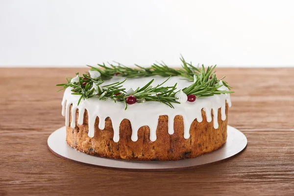 Tasty christmas cake with white icing, rosemary and cranberries on plate on wooden table — Stock Photo