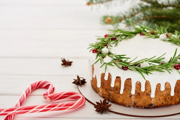 Pastel de Navidad con glaseado en mesa de madera blanca con bastones de caramelo, semillas de anís estrella y ramas de abeto - foto de stock