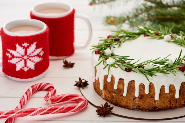 Bastoncini di zucchero, torta di Natale con glassa e due tazze di caffè sul tavolo di legno bianco — Foto stock