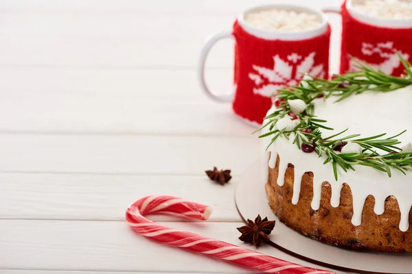 Bastón de caramelo, pastel de Navidad con glaseado y dos tazas de cacao con malvaviscos en una mesa de madera blanca - foto de stock