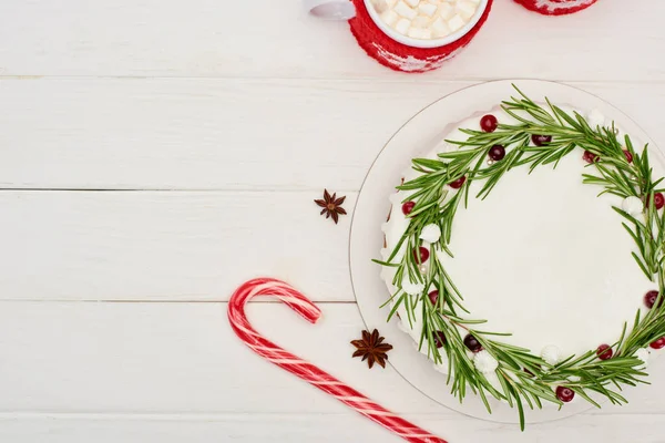 Vista superior de dos tazas de cacao con malvaviscos y pastel de Navidad con glaseado en mesa de madera blanca - foto de stock