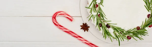 Draufsicht auf Weihnachtskuchen mit Zuckerguss und Rosmarin auf weißem Holztisch mit Zuckerrohr — Stockfoto