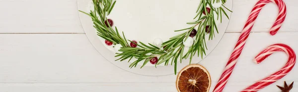 Vista superior de pastel de Navidad con glaseado en mesa de madera blanca con bastones de caramelo y especias - foto de stock