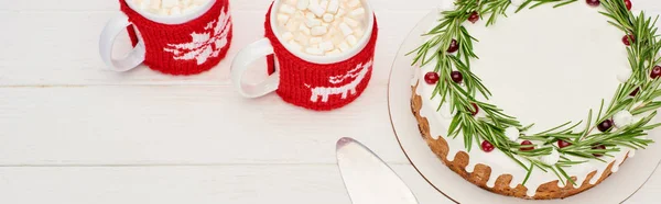 Vista superior del pastel de Navidad con romero y dos tazas de cacao con malvaviscos en la mesa de madera blanca - foto de stock