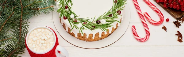 Draufsicht auf Weihnachtskuchen mit Zuckerguss auf weißem Holztisch mit Kakao, Zuckerstangen und Fichtenzweigen — Stockfoto