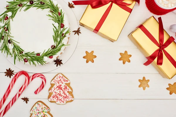 Vista superior de pastel de Navidad, galletas y regalos en mesa de madera blanca - foto de stock