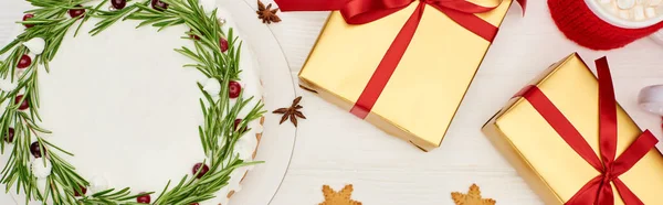 Vista superior de pastel de Navidad, galletas, taza de cacao y cajas de regalo en mesa de madera blanca - foto de stock