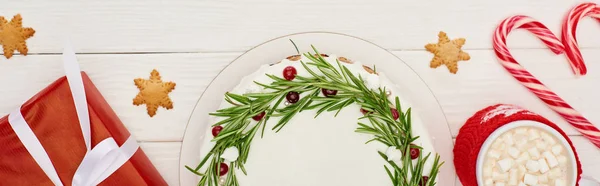 Vista superior de torta de Natal, caixa de presente, biscoitos, bengalas de doces e cacau com marshmallows na mesa de madeira branca — Fotografia de Stock