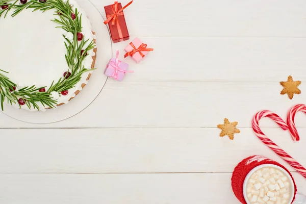 Вид зверху на різдвяний пиріг, подарунки, цукерки та чашку какао з зефіром на білому дерев'яному столі — стокове фото
