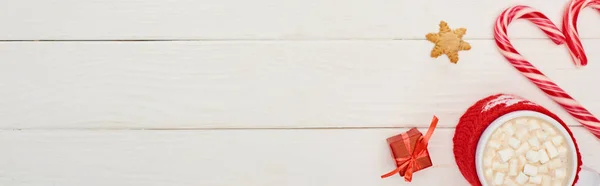Draufsicht auf Weihnachtsbonbons, kleines Geschenk und Tasse Kakao mit Marshmallows auf weißem Holztisch — Stockfoto