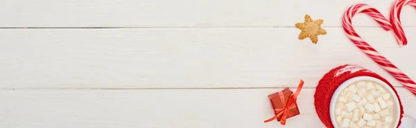 Vue du dessus des cannes de Noël, petit cadeau et tasse de cacao avec guimauves sur table en bois blanc — Photo de stock