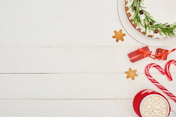 Draufsicht auf Weihnachtskuchen mit Zuckerguss auf weißem Holztisch mit Zuckerstangen, Geschenken und Kakao — Stockfoto