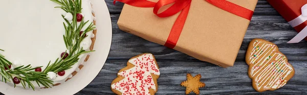 Vista superior de pastel de Navidad, galletas dulces y cajas de regalo en mesa de madera oscura - foto de stock