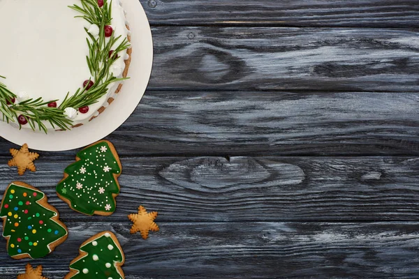 Vista superior del pastel de Navidad y galletas de árbol de Navidad en la mesa de madera oscura - foto de stock