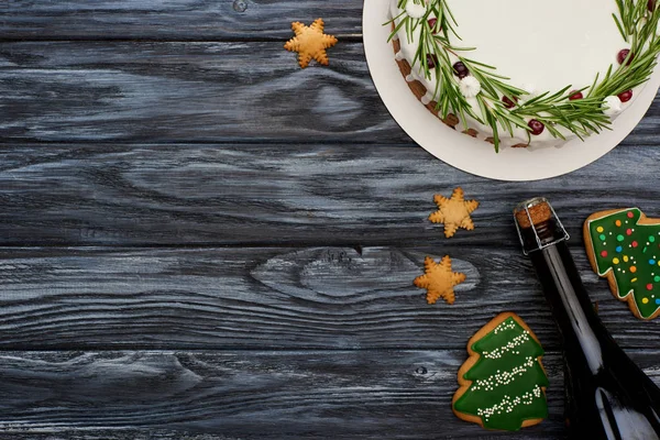 Vista superior del pastel de Navidad, botella de champán y galletas de árbol de Navidad en la mesa de madera oscura - foto de stock