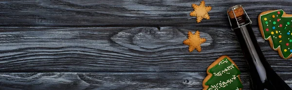 Top view of bottle of champagne and christmas tree cookies on dark wooden table — Stock Photo