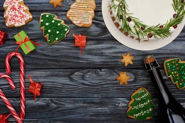 Vista superior da torta de Natal, garrafa de champanhe, bengalas de doces, pequenos presentes e biscoitos na mesa de madeira escura — Fotografia de Stock