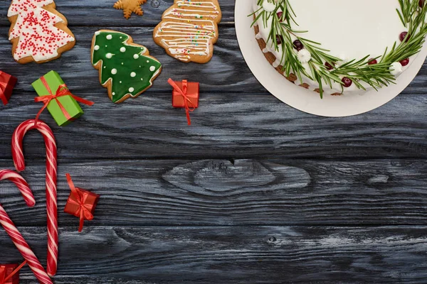 Vista superior da torta de Natal, bengalas doces, pequenos presentes e biscoitos na mesa de madeira escura — Fotografia de Stock