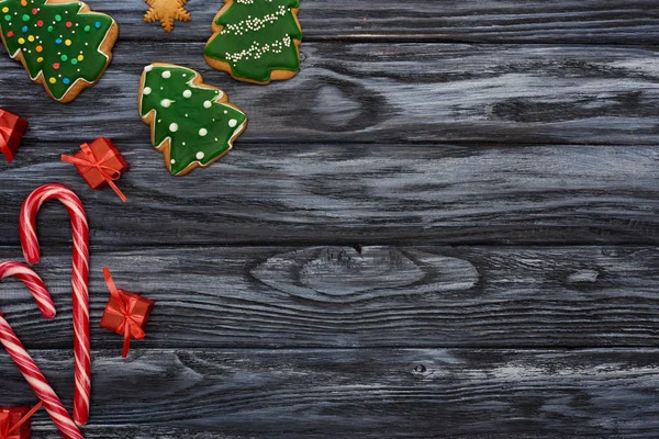 Vista superior de pequeños regalos, bastones de caramelo y galletas de árbol de Navidad en la mesa de madera oscura - foto de stock