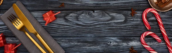 Вид сверху на вилку и нож на салфетке с маленькими подарками и леденцами на темном деревянном столе — стоковое фото